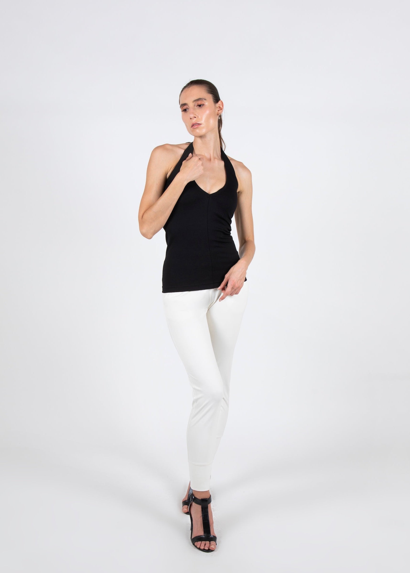 Woman wearing a black tank top and white pants on a white background