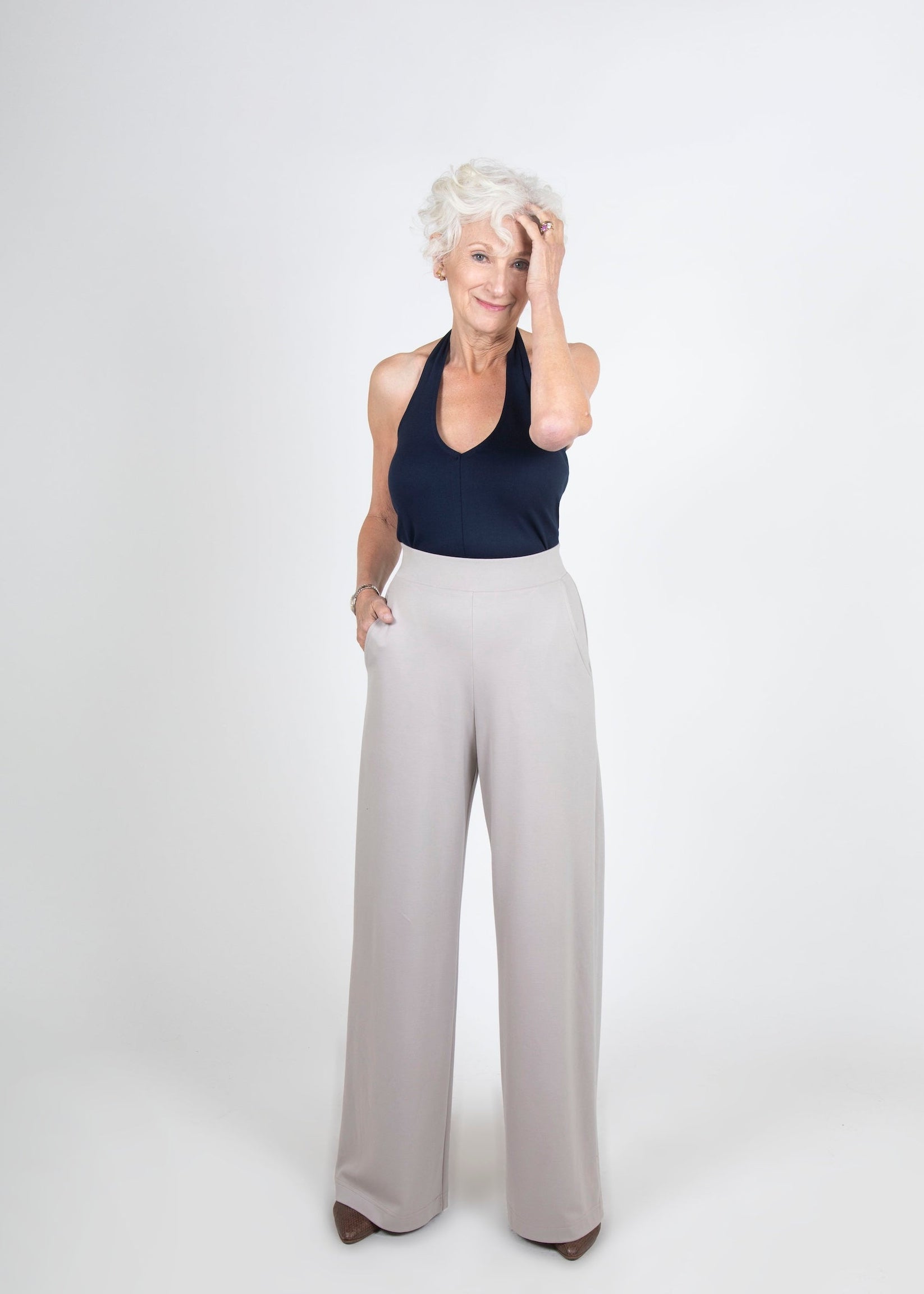 Woman wearing a navy halter top and taupe wide-leg pants on a white background