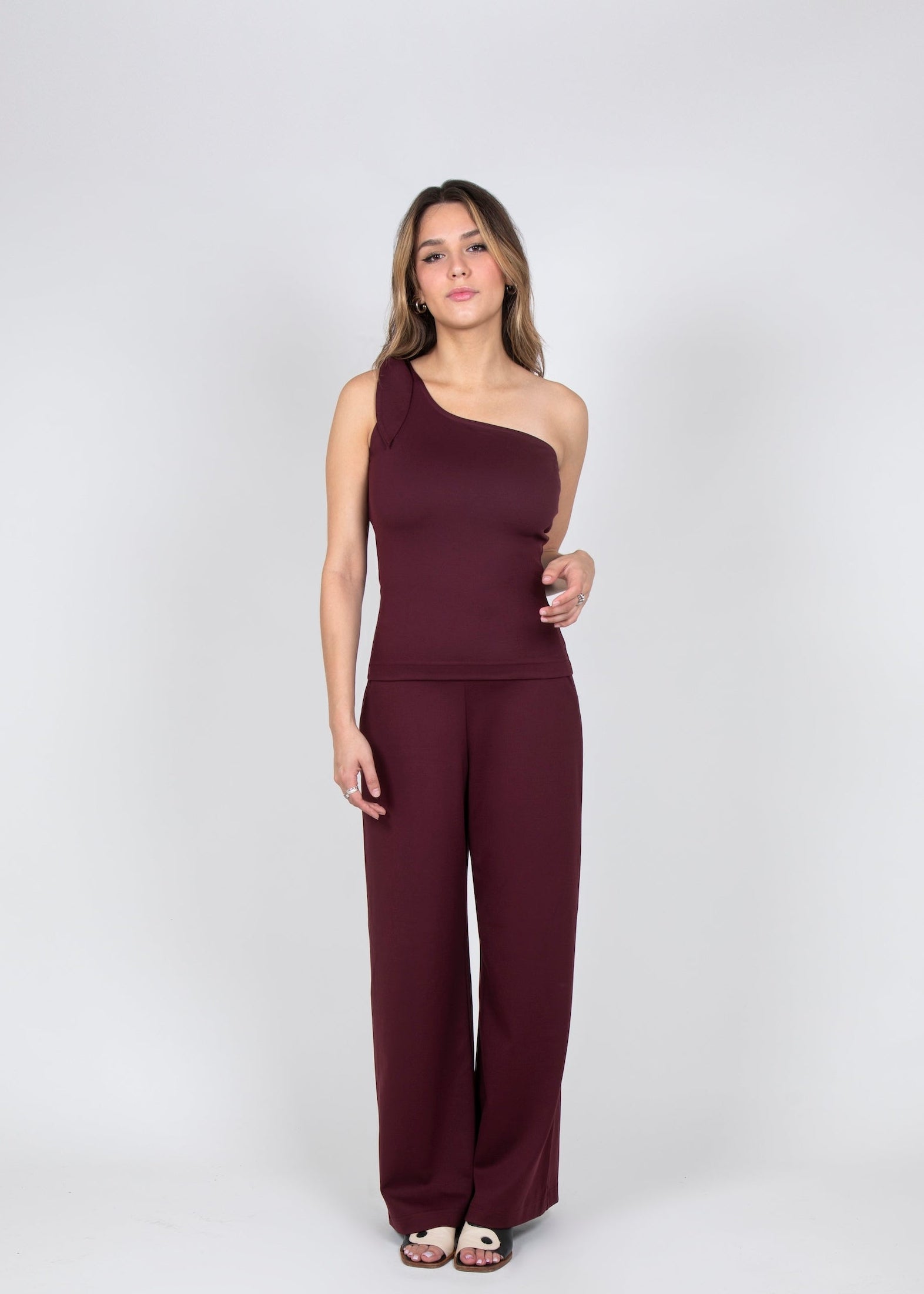 Woman wearing a burgundy one-shoulder jumpsuit on a white background