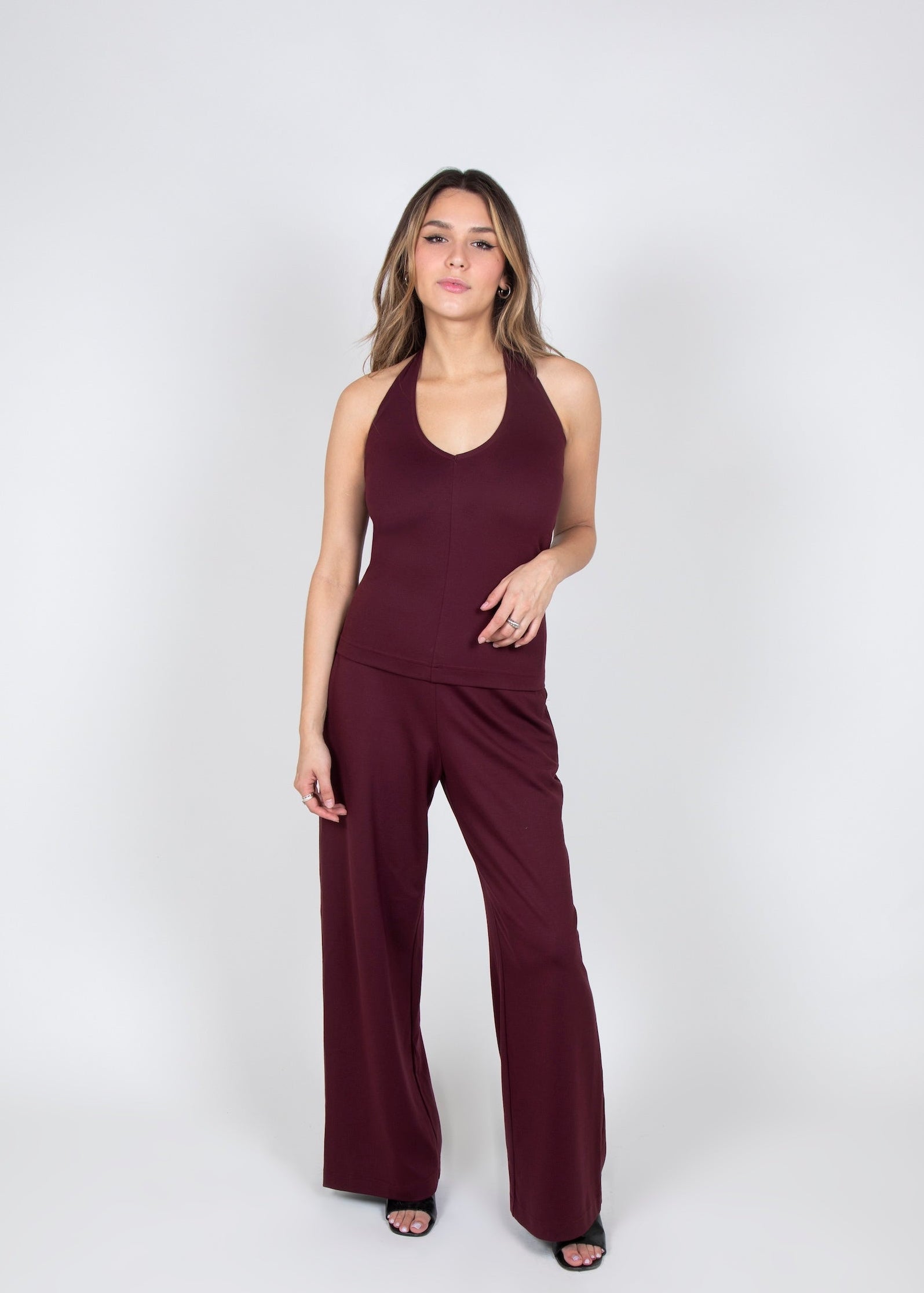 Woman wearing a burgundy halter and wide leg pants on a white background