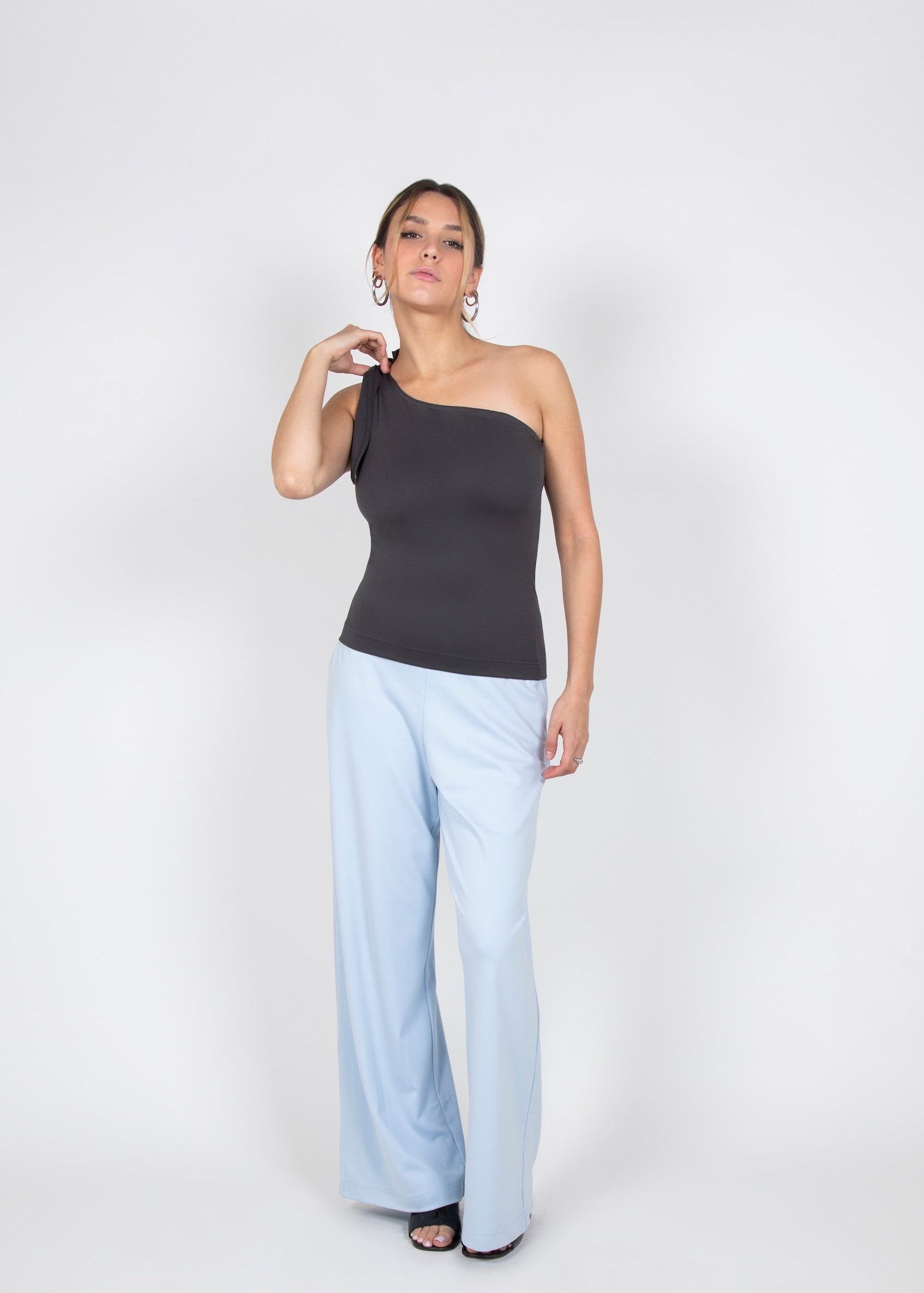 Woman wearing a dark gray one-shoulder top and light blue pants on a white background