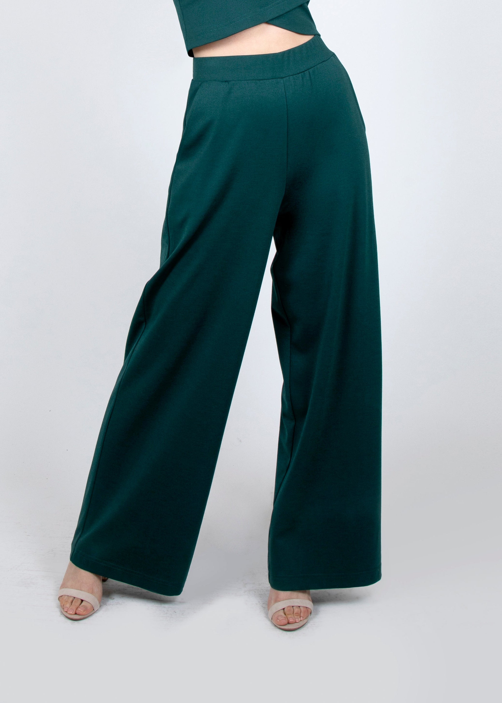 A person wearing high-waisted emerald green wide leg palazzo pants with pockets, paired with a crop top, standing against a neutral background.