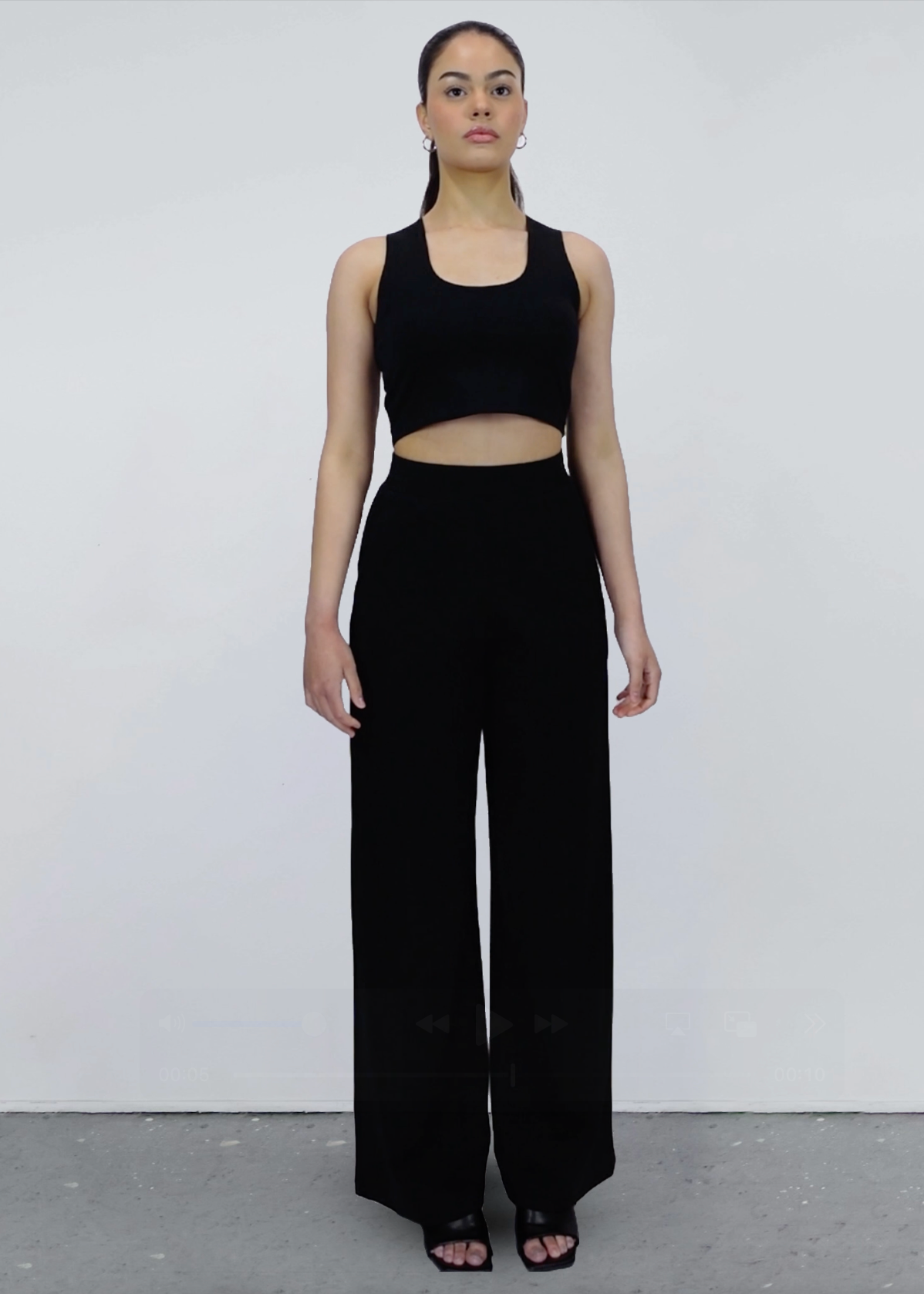 Woman wearing a black sleeveless top and wide-leg pants against a white background