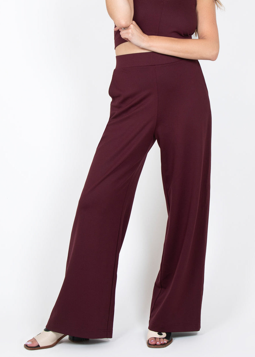 A person wearing high-waisted burgundy wide-leg palazzo pants, paired with a top and sandals.