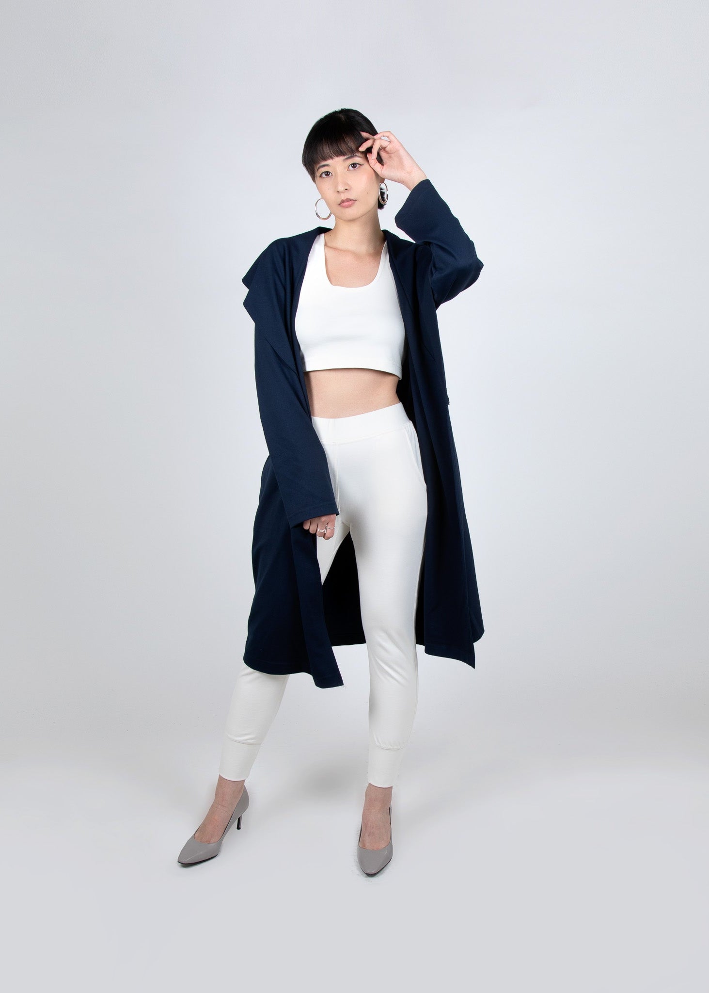 A woman wearing a navy shawl collar trench coat with a cream crop top and jogger set.